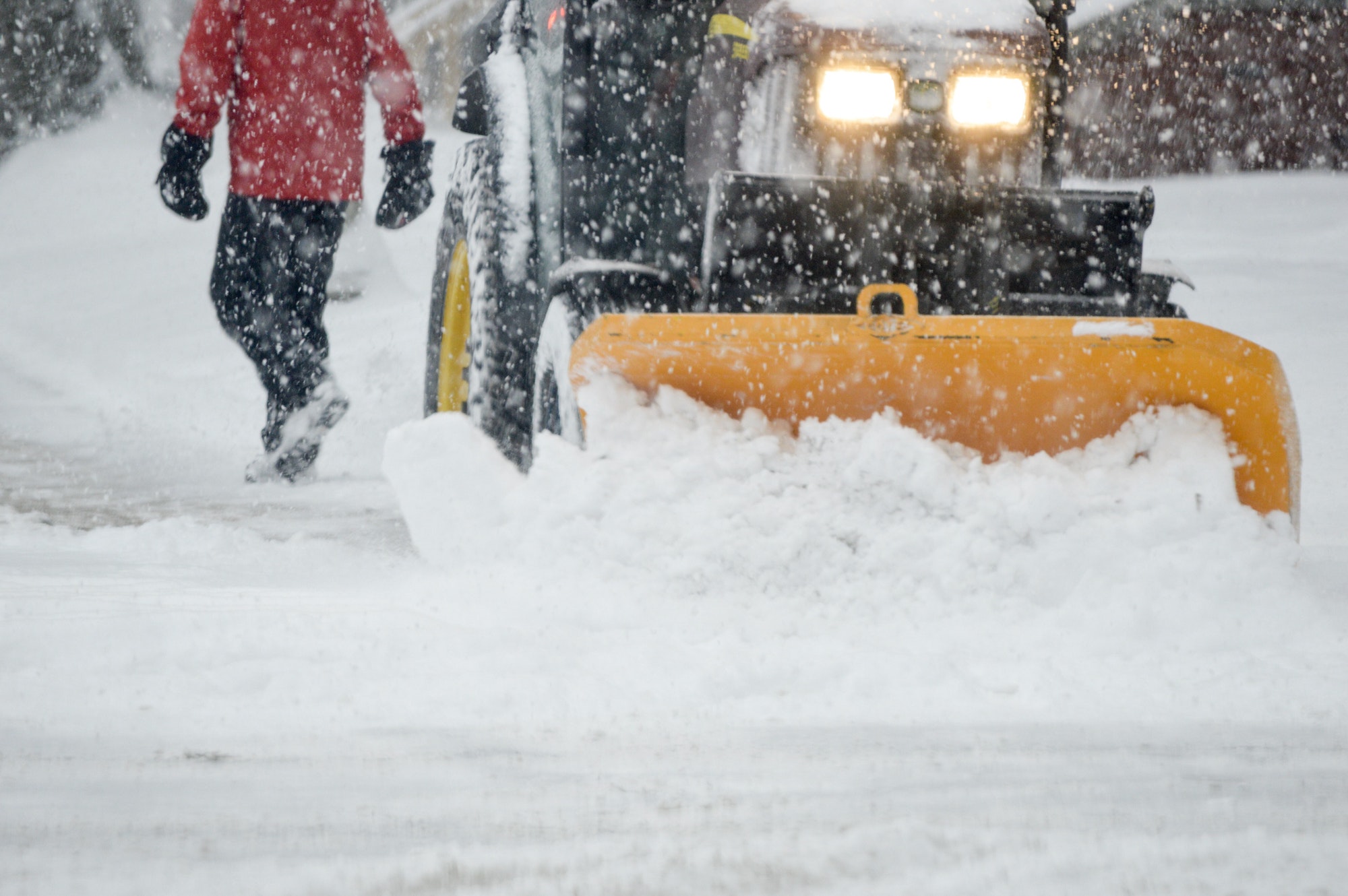 A person walking in a Snowstorm with a snow plow clearing street in heavy snow fall urban winter